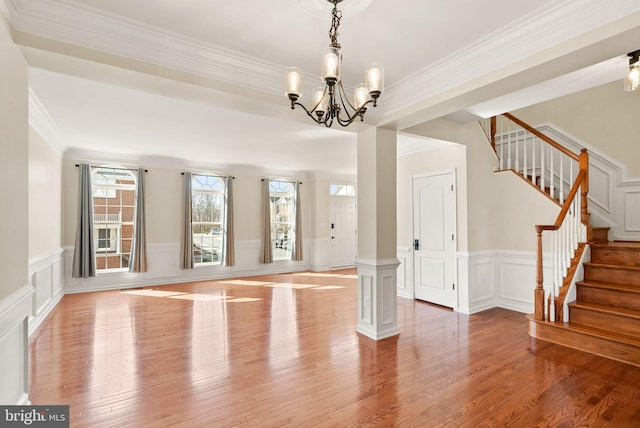 interior space featuring a notable chandelier, a decorative wall, ornamental molding, wood finished floors, and stairs