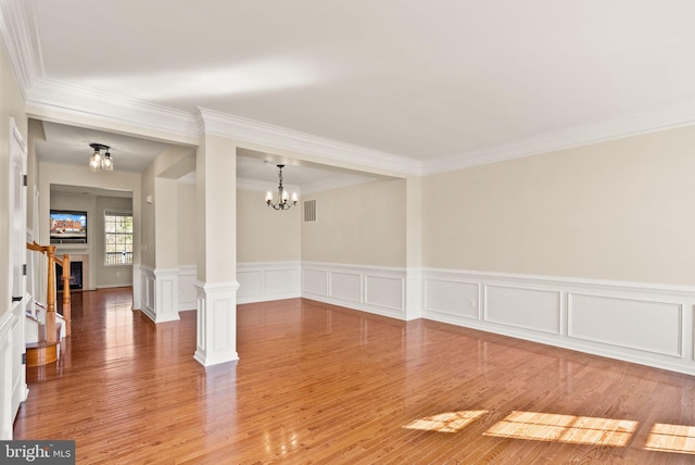 spare room with light wood finished floors, a fireplace, decorative columns, and a notable chandelier