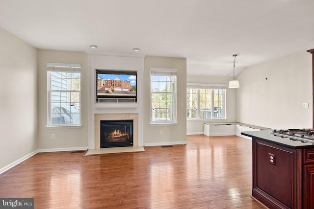 unfurnished living room featuring visible vents, wood-type flooring, a fireplace with flush hearth, and a wealth of natural light