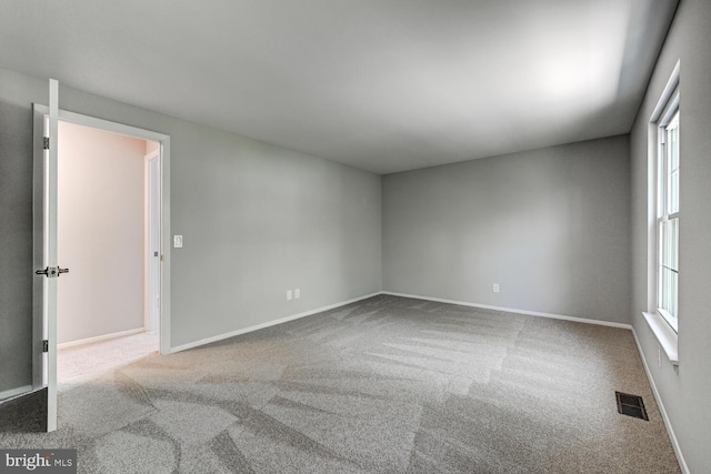 carpeted spare room with visible vents, baseboards, and plenty of natural light