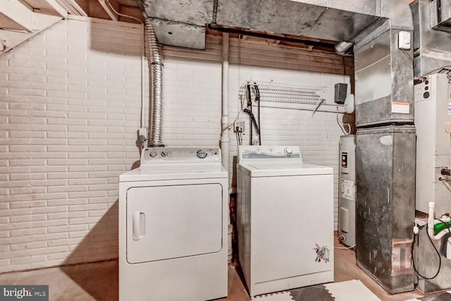 laundry room with laundry area, brick wall, washer and dryer, and electric water heater