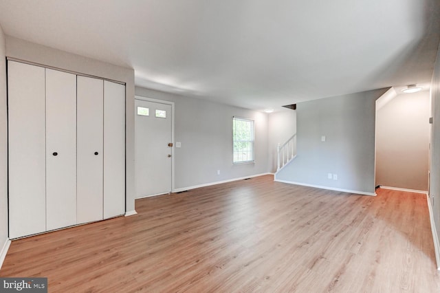 unfurnished living room with stairway, baseboards, and light wood finished floors