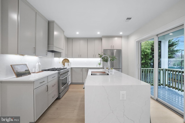 kitchen with a sink, gray cabinetry, custom range hood, appliances with stainless steel finishes, and a center island