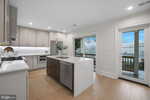 kitchen featuring visible vents, a center island with sink, light stone counters, light wood-style flooring, and appliances with stainless steel finishes