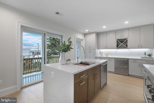 kitchen featuring visible vents, an island with sink, light wood-style floors, and a sink