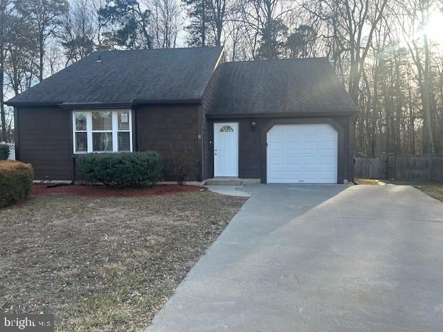 ranch-style house featuring a garage, concrete driveway, roof with shingles, and fence