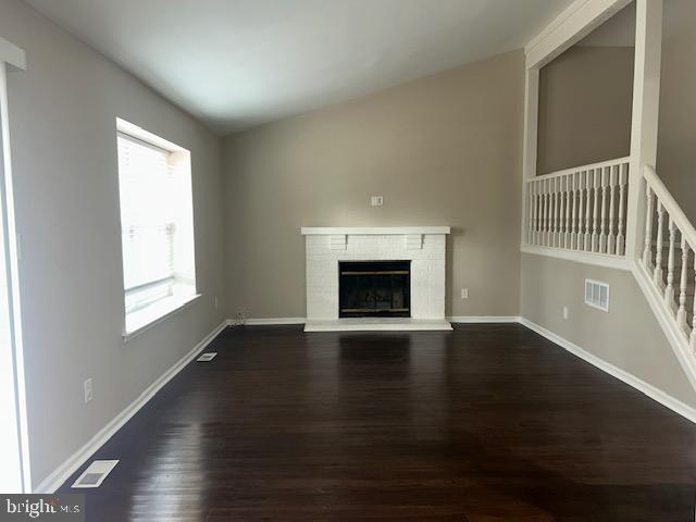 unfurnished living room featuring dark wood-type flooring, a brick fireplace, visible vents, and baseboards