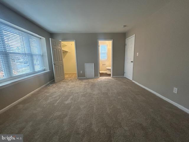 unfurnished bedroom featuring a walk in closet, a closet, carpet flooring, and baseboards