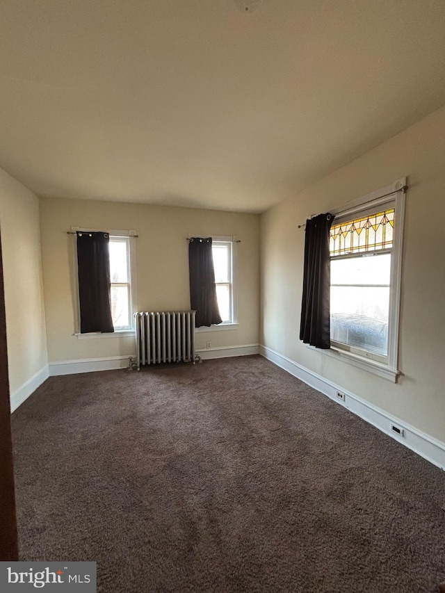 unfurnished room with radiator heating unit, dark carpet, and baseboards