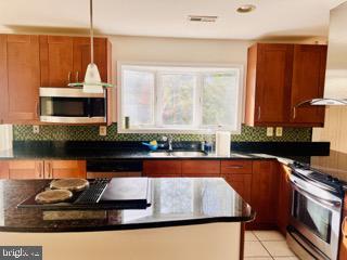 kitchen featuring light tile patterned flooring, stainless steel appliances, a sink, tasteful backsplash, and dark countertops