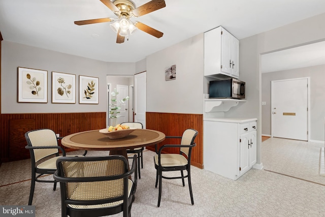 dining room with a ceiling fan, a wainscoted wall, and wood walls