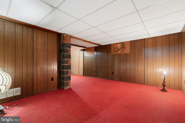 finished basement featuring wood walls, a drop ceiling, carpet flooring, and visible vents