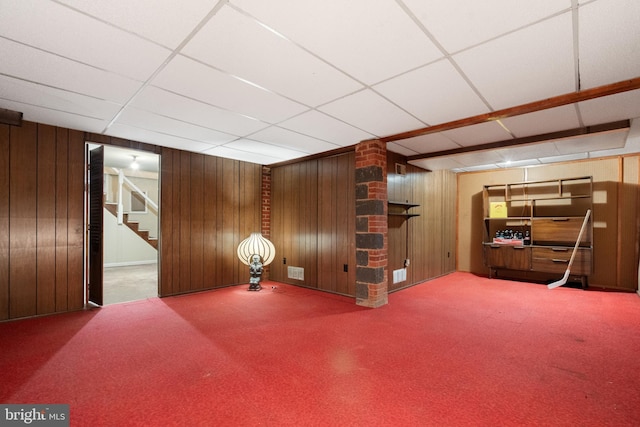 finished basement featuring wood walls, stairway, carpet, and a drop ceiling