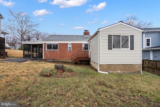 back of house with brick siding, a chimney, a lawn, a sunroom, and fence