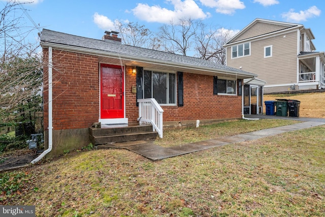 view of front facade featuring roof with shingles, a front yard, a chimney, and brick siding