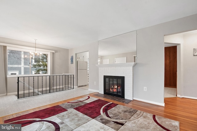 living area featuring a notable chandelier, a fireplace, baseboards, and wood finished floors