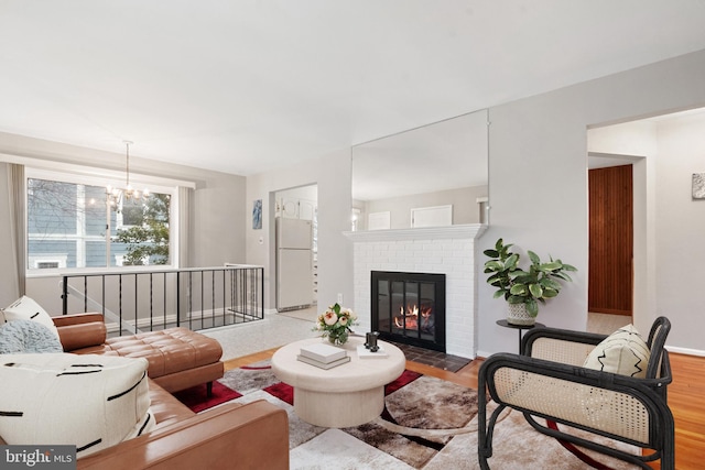 living room with a chandelier, a brick fireplace, wood finished floors, and baseboards