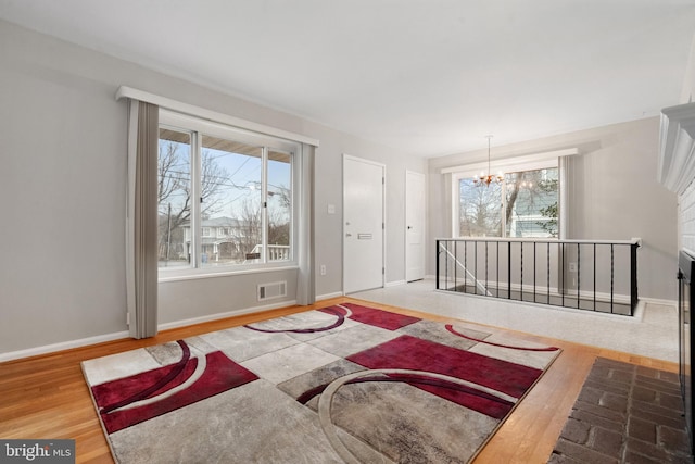 living room featuring baseboards, wood finished floors, visible vents, and a notable chandelier