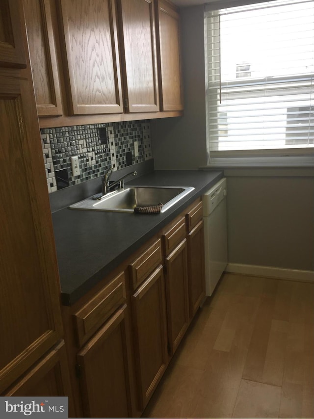 kitchen featuring a sink, baseboards, decorative backsplash, dishwasher, and dark countertops