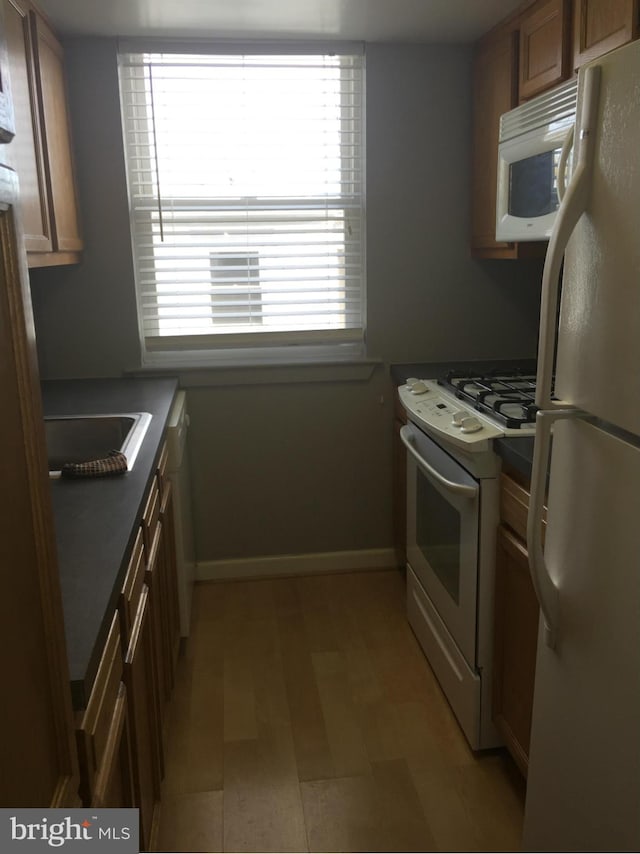 kitchen with white appliances, dark countertops, brown cabinets, and baseboards