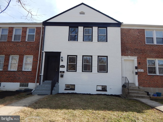 townhome / multi-family property with entry steps, brick siding, and a front lawn