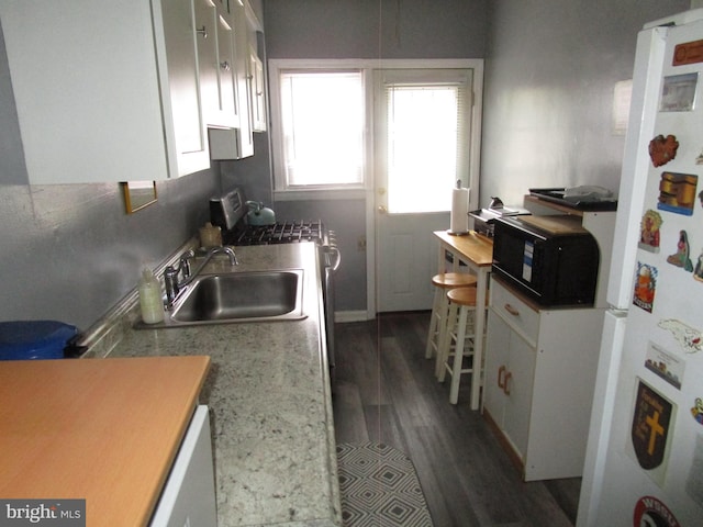 kitchen with black microwave, dark wood-type flooring, freestanding refrigerator, white cabinetry, and a sink