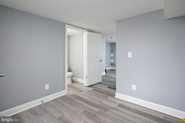 unfurnished bedroom featuring ensuite bathroom, baseboards, and wood finished floors