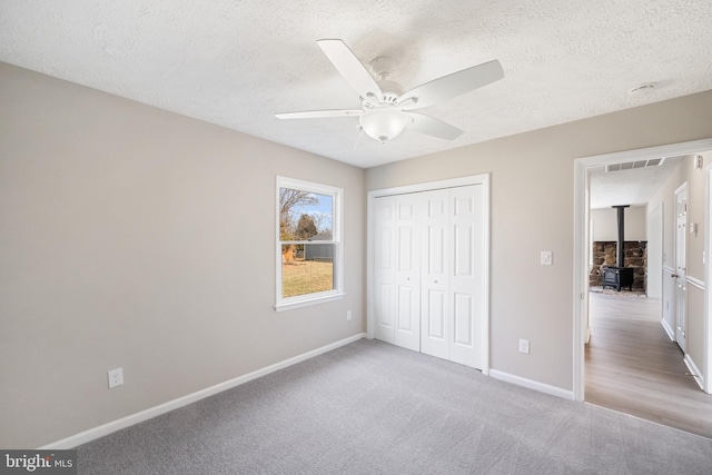 unfurnished bedroom featuring carpet, a closet, a wood stove, a textured ceiling, and baseboards