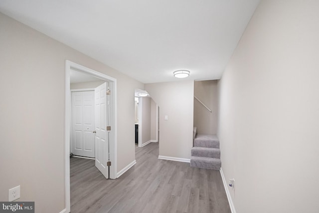 hallway featuring light wood finished floors, stairway, and baseboards