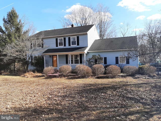 traditional home with covered porch, a chimney, and roof with shingles