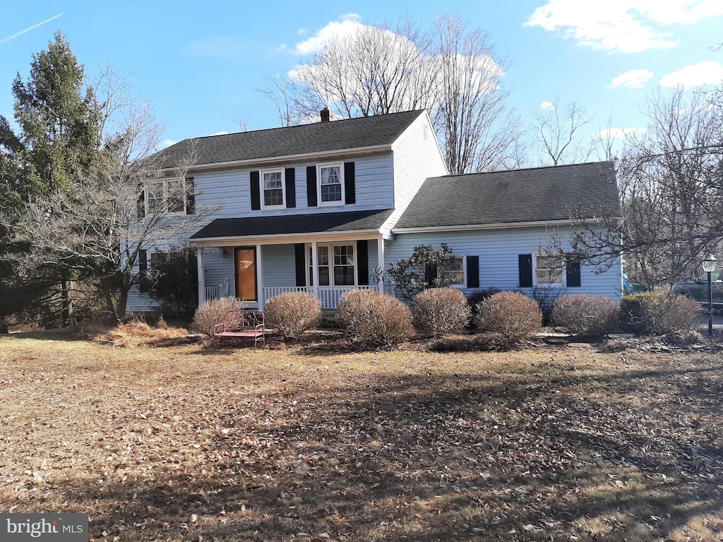 traditional-style home featuring covered porch, roof with shingles, and a chimney