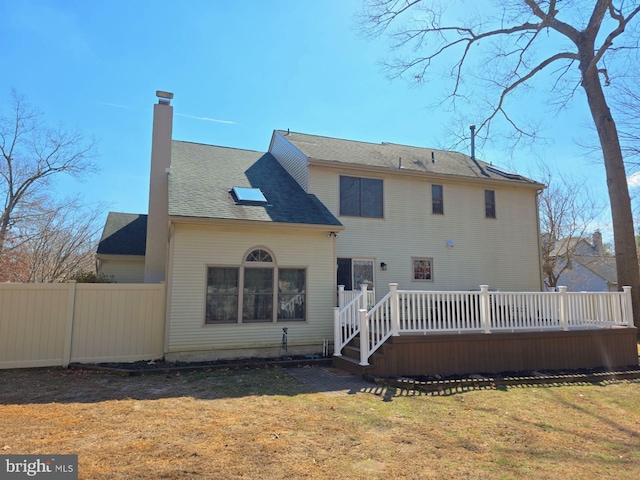 back of house with a deck, a yard, a chimney, and fence