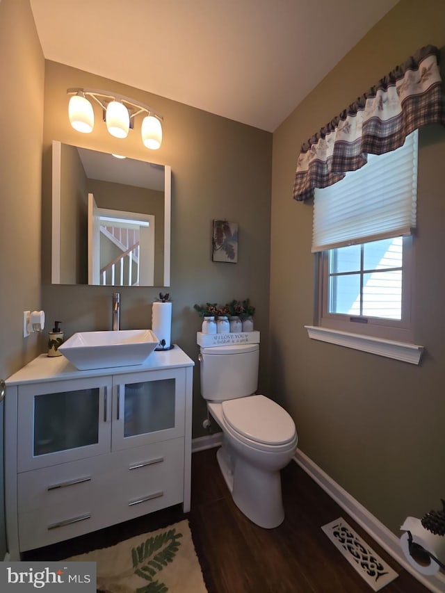 half bathroom featuring baseboards, visible vents, toilet, wood finished floors, and vanity