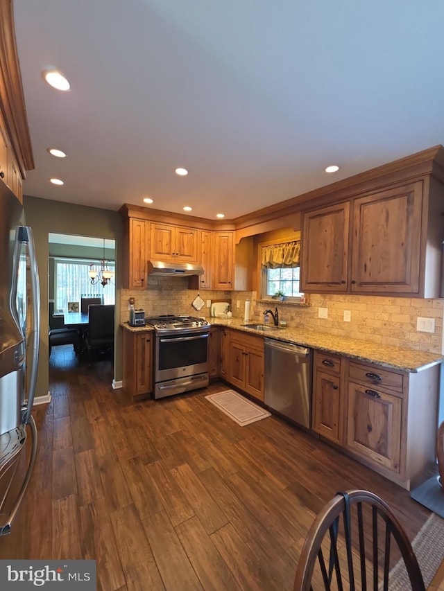 kitchen featuring dark wood finished floors, brown cabinets, stainless steel appliances, under cabinet range hood, and a sink