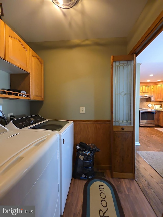 laundry area with cabinet space, wooden walls, wainscoting, dark wood-type flooring, and washing machine and clothes dryer