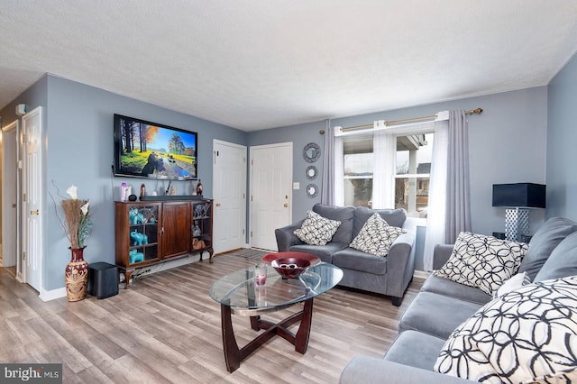 living area with light wood-style flooring, baseboards, and a textured ceiling