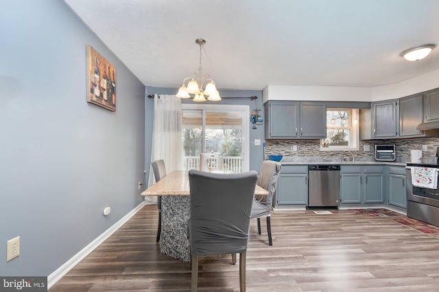 kitchen with light wood-style flooring, an inviting chandelier, stainless steel appliances, light countertops, and backsplash