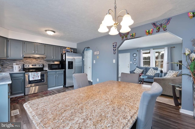 kitchen featuring arched walkways, under cabinet range hood, light countertops, appliances with stainless steel finishes, and tasteful backsplash