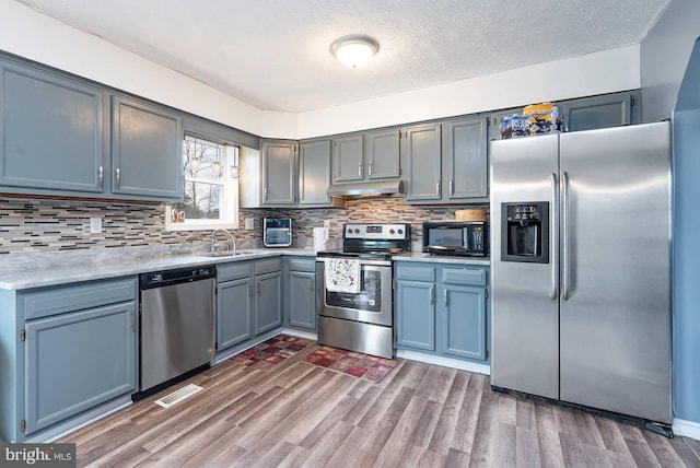 kitchen with under cabinet range hood, wood finished floors, a sink, light countertops, and appliances with stainless steel finishes