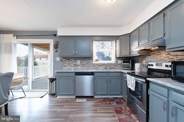 kitchen with light countertops, appliances with stainless steel finishes, a sink, and under cabinet range hood