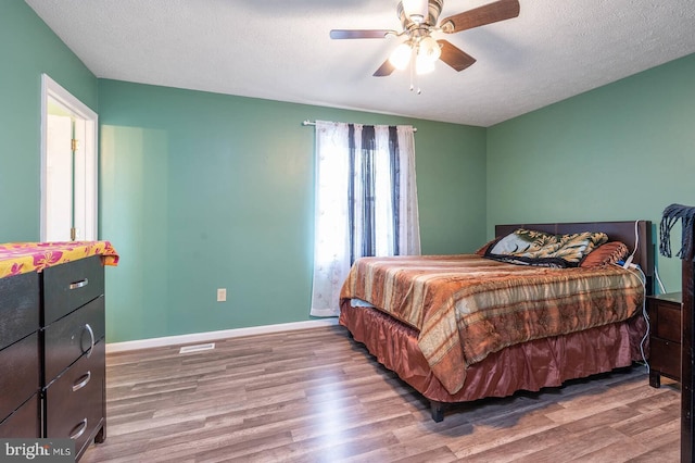 bedroom featuring a ceiling fan, a textured ceiling, baseboards, and wood finished floors