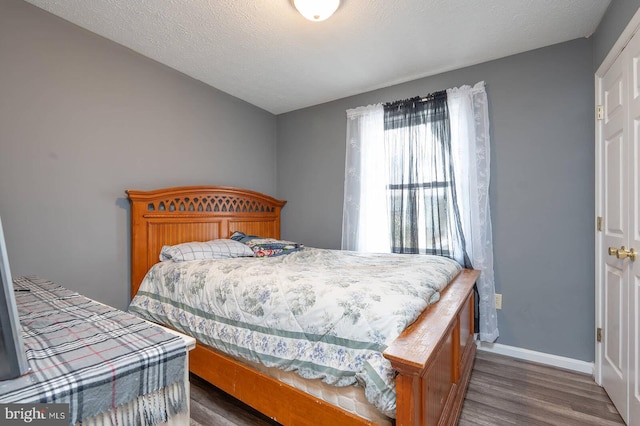 bedroom with a textured ceiling, baseboards, and wood finished floors