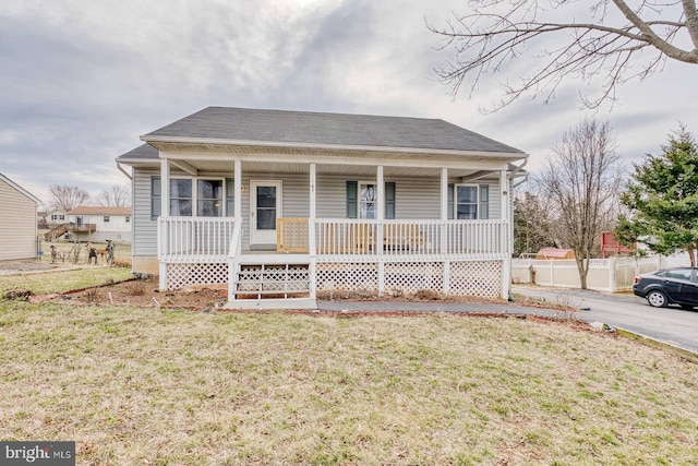 bungalow with covered porch, roof with shingles, fence, and a front lawn