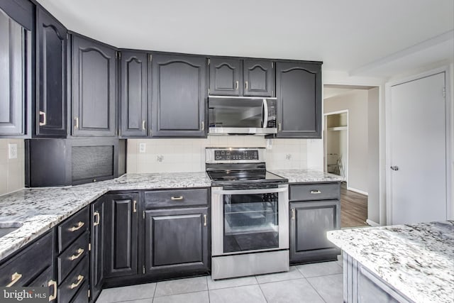 kitchen featuring light tile patterned floors, appliances with stainless steel finishes, light stone countertops, and tasteful backsplash