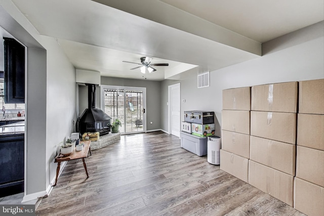 sitting room featuring baseboards, visible vents, ceiling fan, wood finished floors, and a wood stove