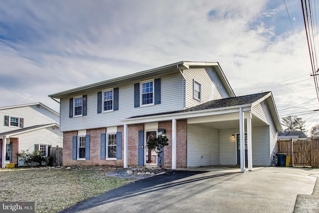 view of front facade featuring driveway, fence, an attached carport, and brick siding