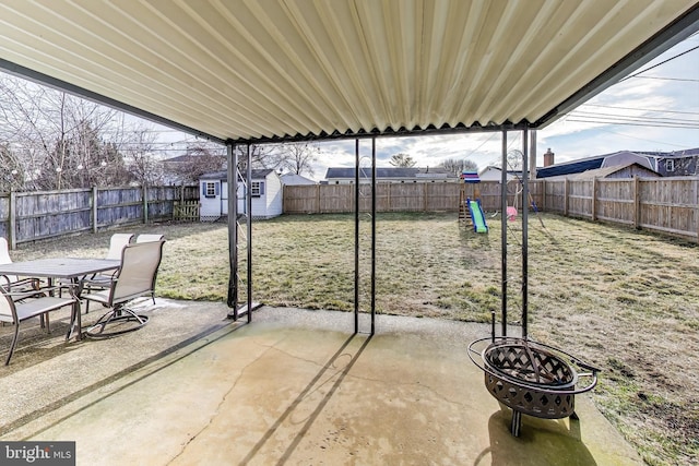 view of patio / terrace with a playground, a storage shed, a fenced backyard, an outdoor structure, and a fire pit