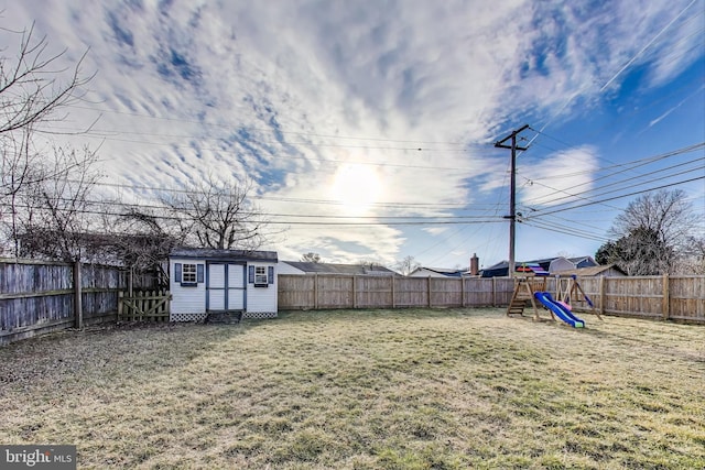 view of yard with a fenced backyard, a shed, a playground, and an outbuilding