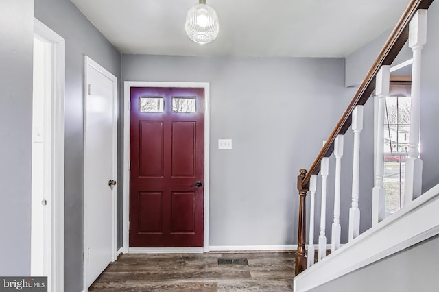 foyer featuring baseboards, visible vents, stairway, and wood finished floors