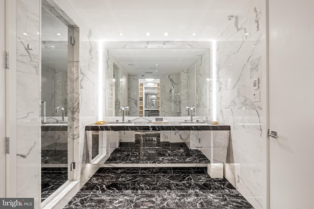 bathroom featuring stone wall, marble finish floor, and a sink